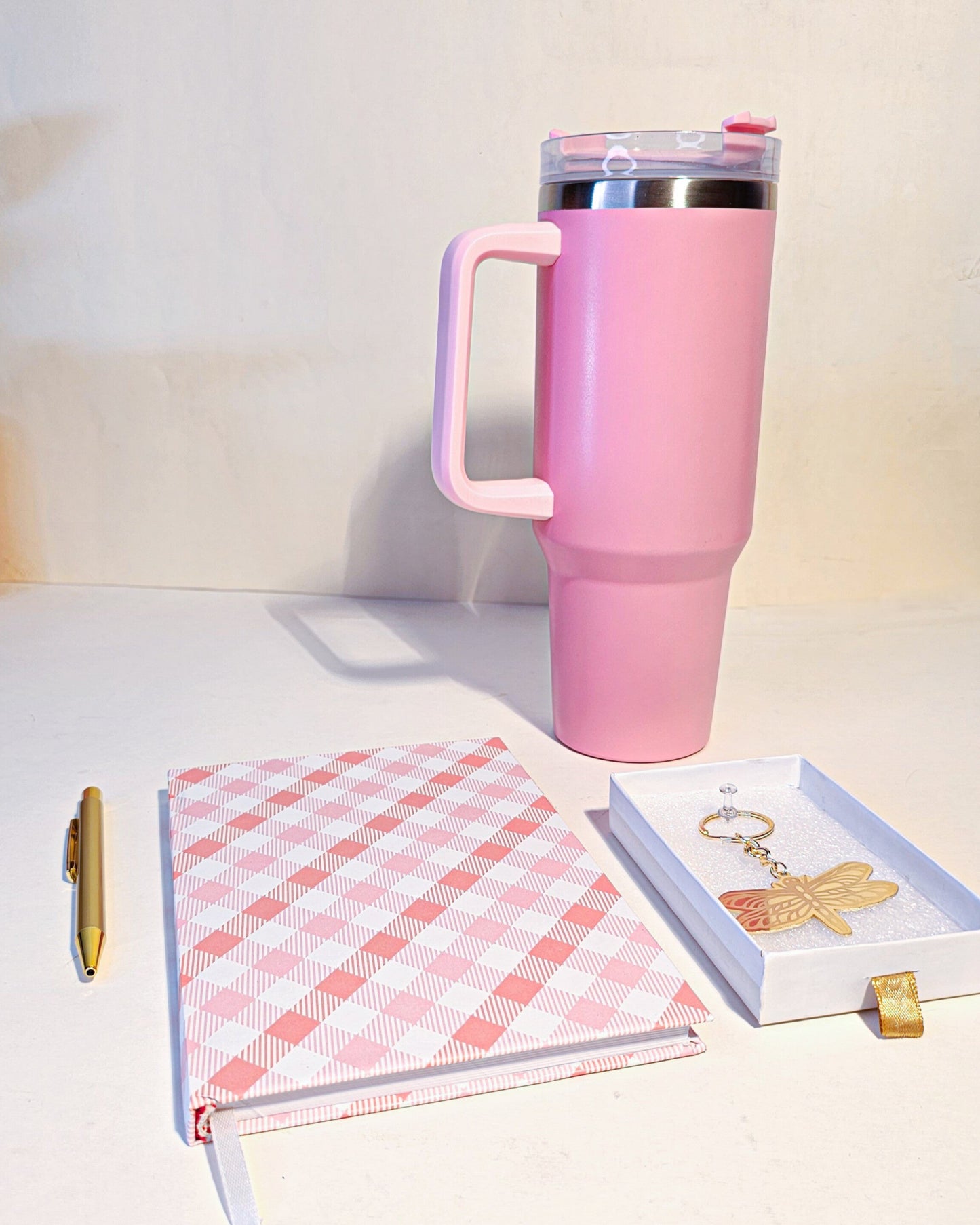 Pink travel mug with a notebook and keychain on a light surface