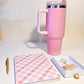 Pink travel mug with a notebook and keychain on a light surface